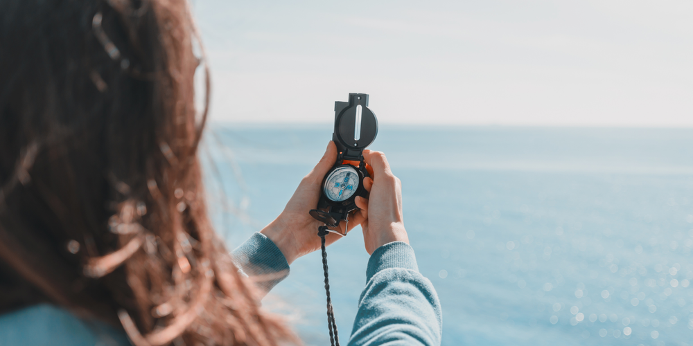 une femme tient une boussole face à la mer